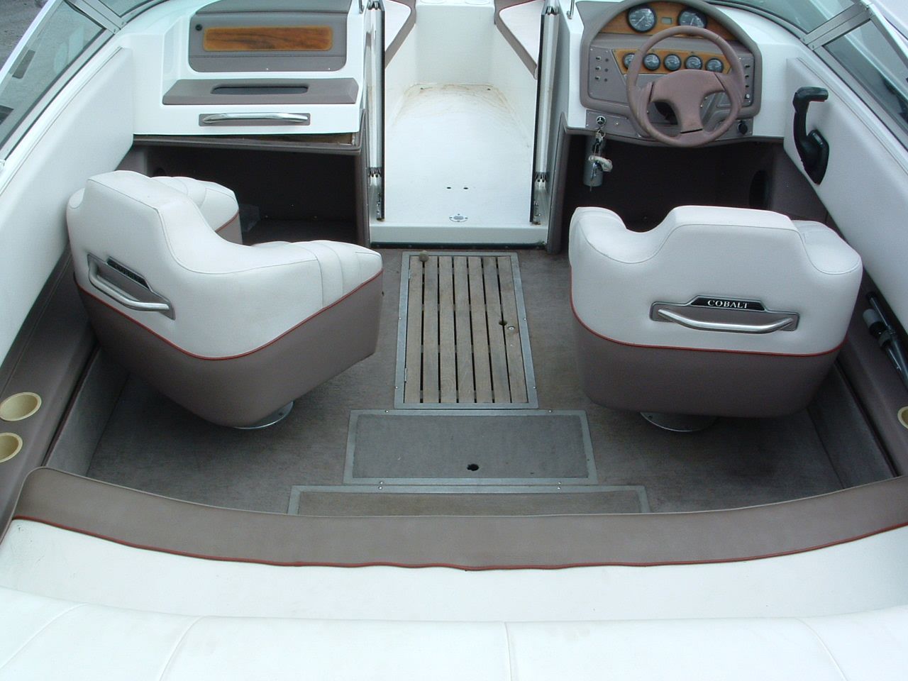The inside of a boat with a steering wheel and two chairs