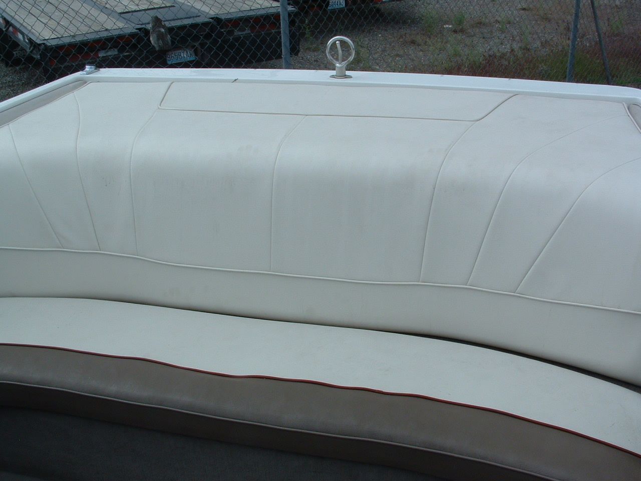 A white boat with a red trim is parked in front of a chain link fence