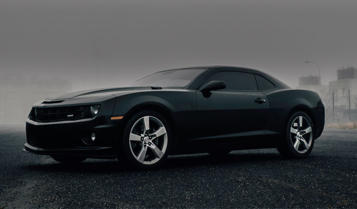 Black Chevrolet Camaro parked on a dark, wet road with foggy backdrop. | Stu's Collision Center