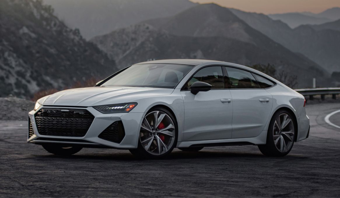White Audi RS 7 on a winding road with mountains in the background. | Stu's Collision Center