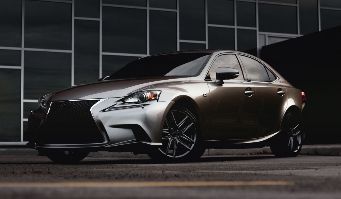 Silver and bronze Lexus sedan parked in front of a modern building with dark windows. | Stu's Collision Center