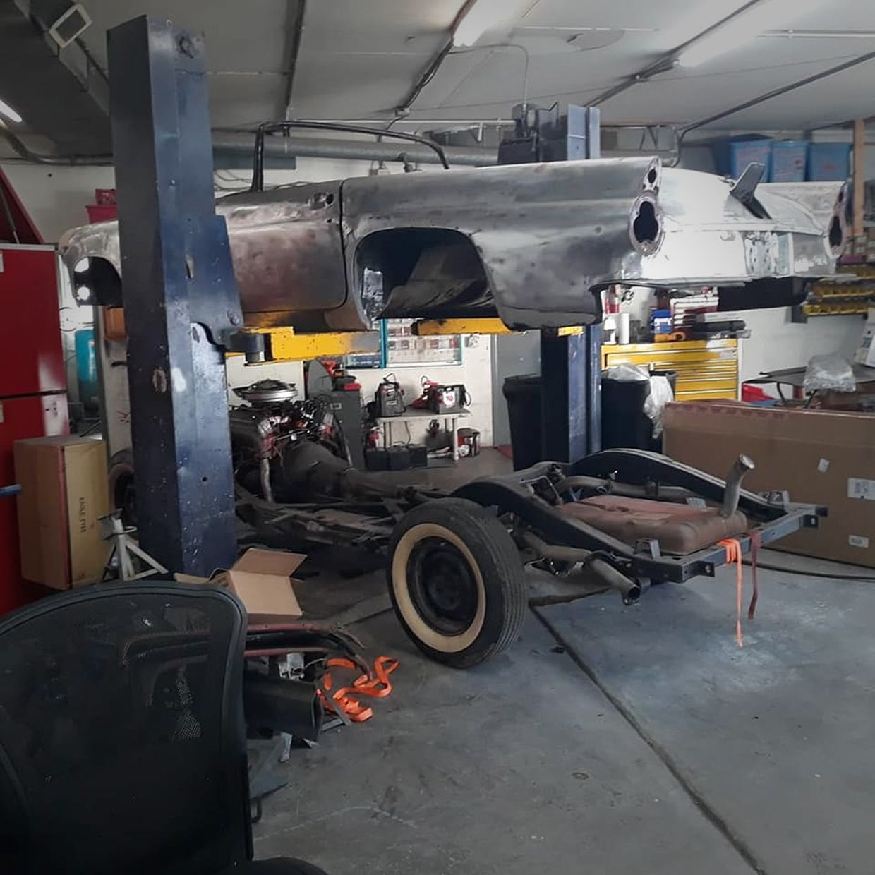 A classic car restoration in progress at a workshop, with the body mounted on a lift above the chassis. | Stu's Collision Center