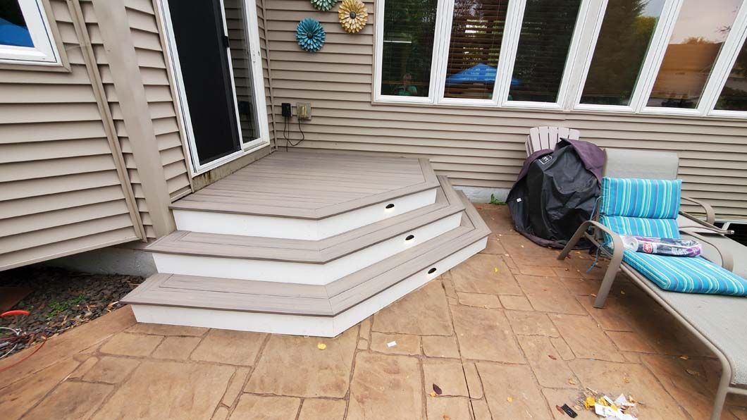 A patio with stairs and a chair in front of a house.
