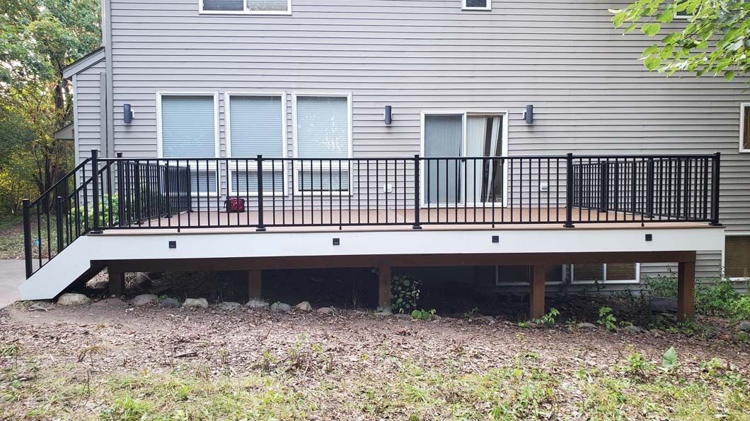 A large deck with a black railing is in front of a house.