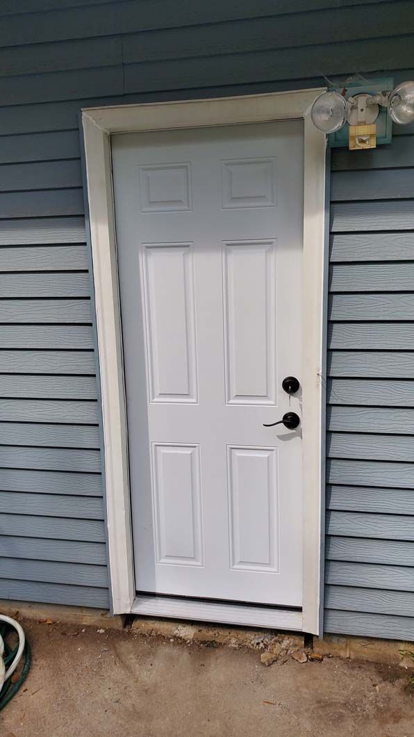 A white door is sitting on the side of a blue house.