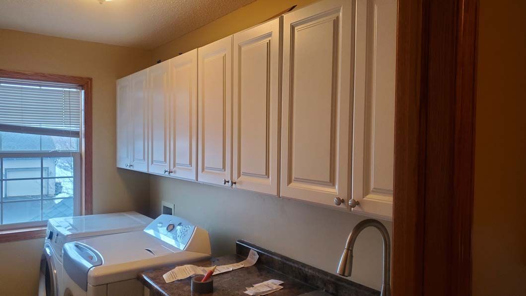 A laundry room with white cabinets , a washer and dryer , a sink , and a window.