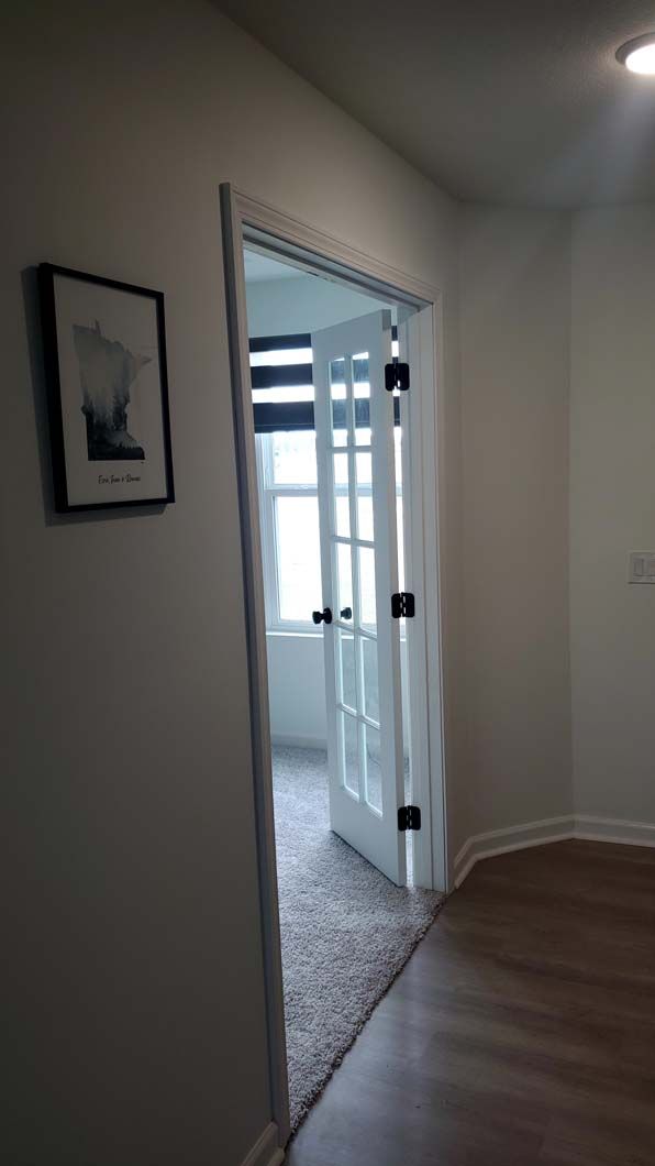 A hallway with a picture on the wall and a door leading to a bedroom.