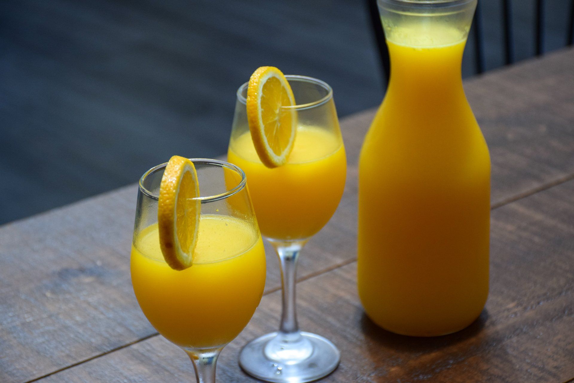 Two glasses of orange juice and a pitcher of orange juice on a wooden table.