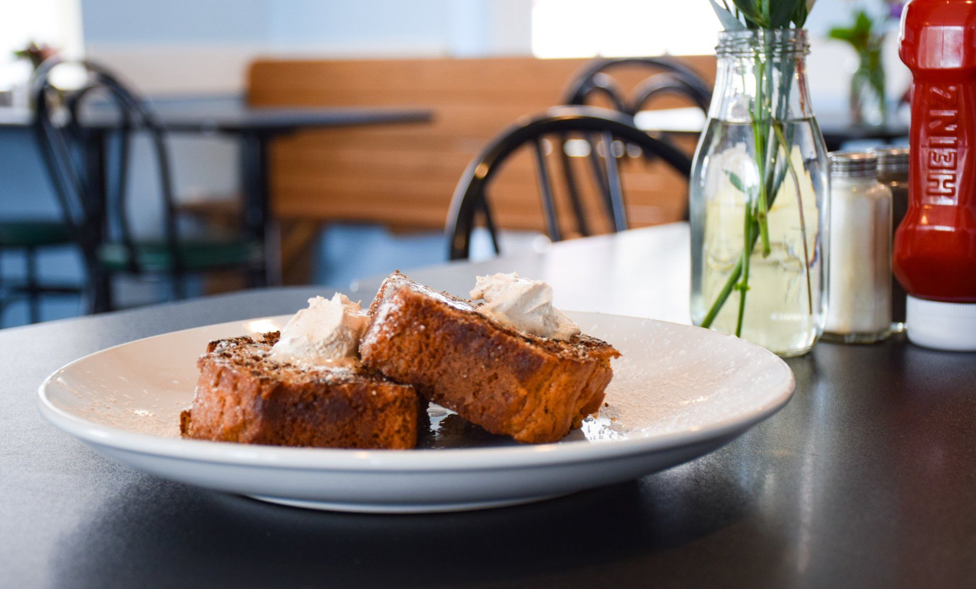 A plate of french toast with whipped cream on a table in a restaurant.