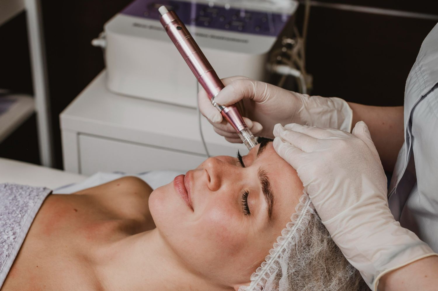 Woman receiving microblading treatment on her eyebrow. A gloved hand holds a pen-like tool near her face.