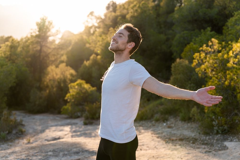 A man is standing in the woods with his arms outstretched.