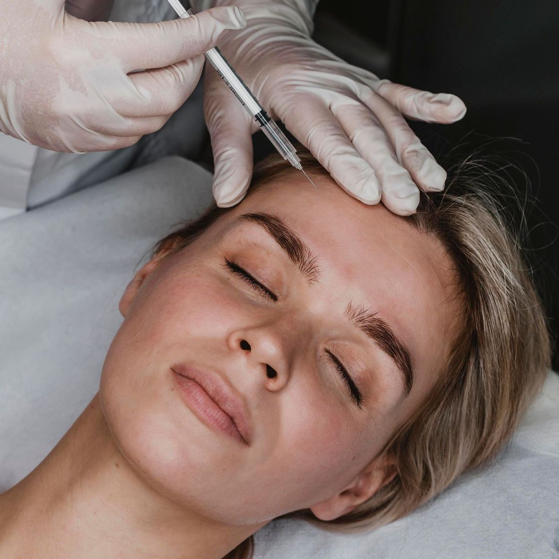 A woman is getting a botox injection on her forehead