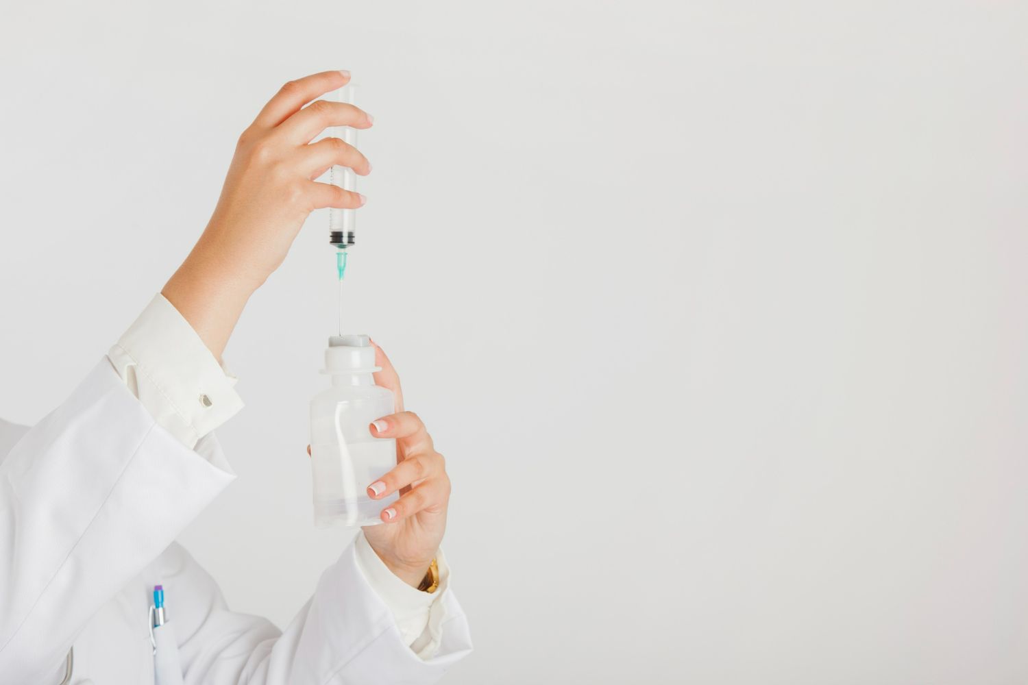 Person in a white lab coat filling a syringe from a medication vial.