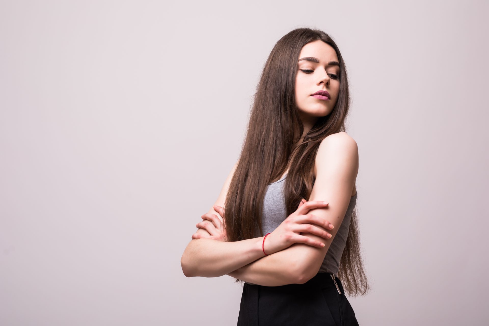 A woman with long hair is standing with her arms crossed and her eyes closed.