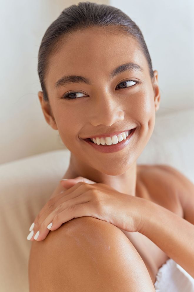 A woman is touching her face with her hand and smiling.