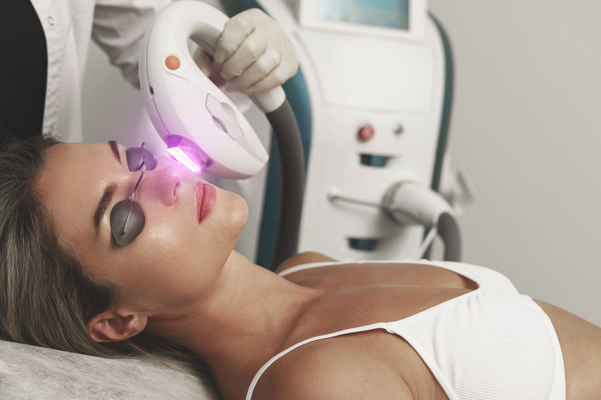 Woman receiving laser facial treatment; bright light, medical setting.