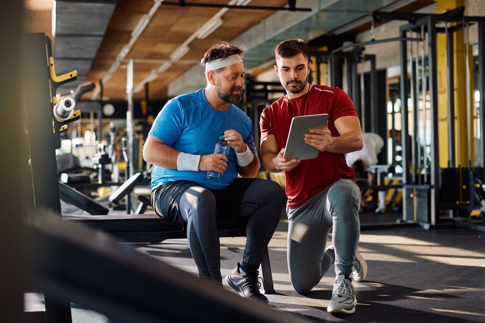 Two men are looking at a tablet in a gym.