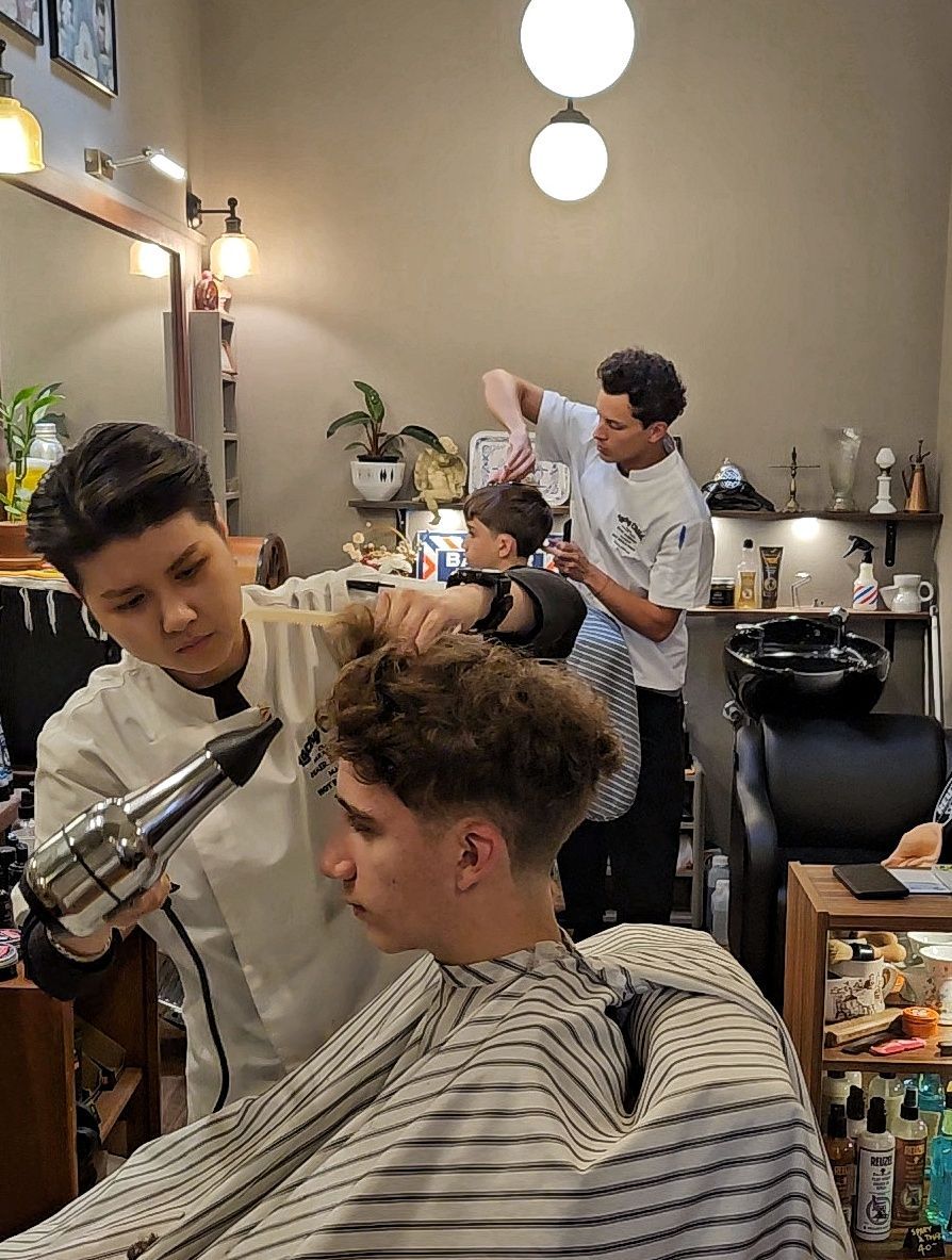 Barbershop Scene With a Stylist Trimming a Client’s Curly Hair in a Striped Cape — Lucky Child Barber Shop In Hobart, TAS
