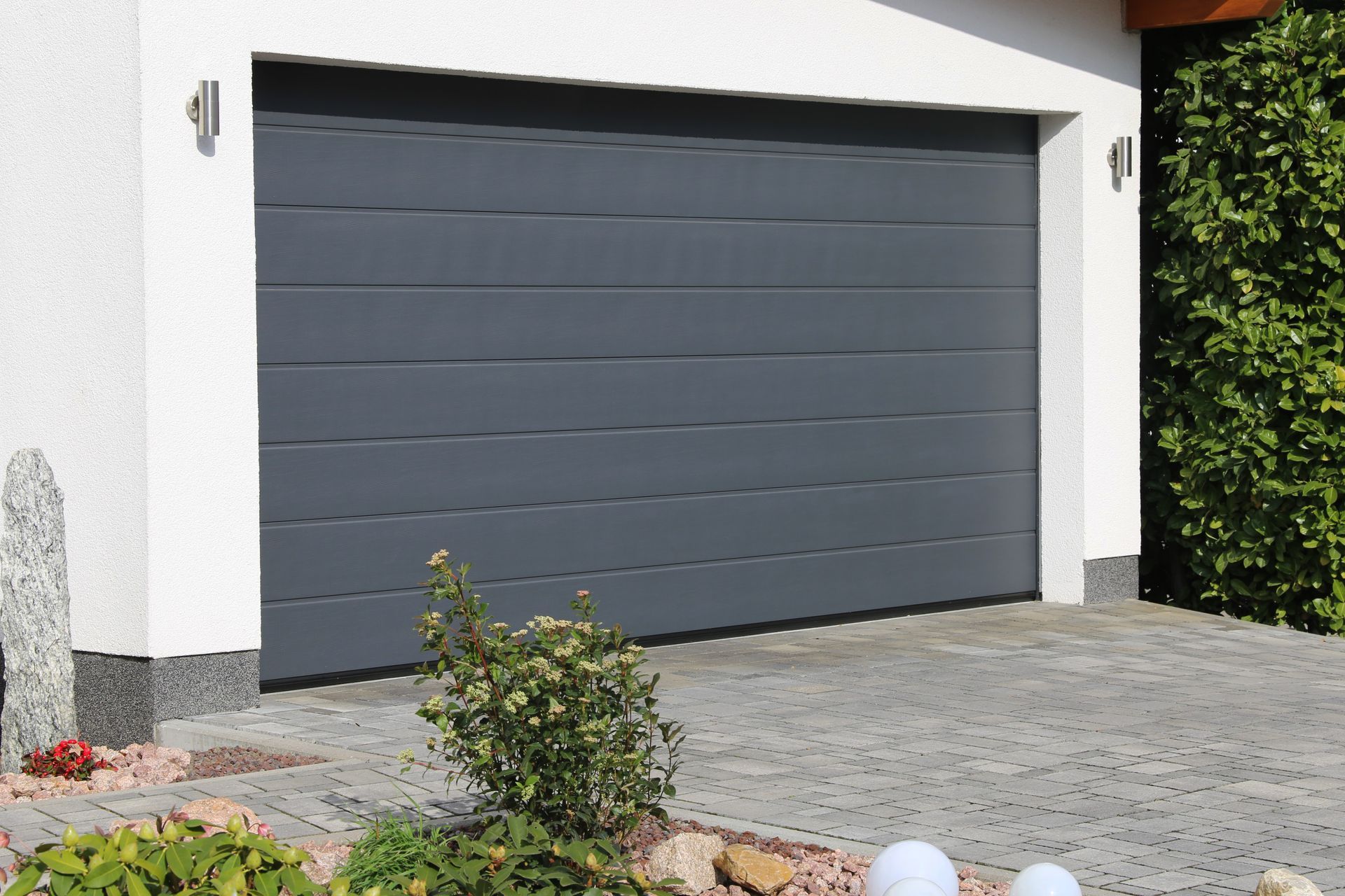 Gray garage door on a white house with a paved driveway and green hedge