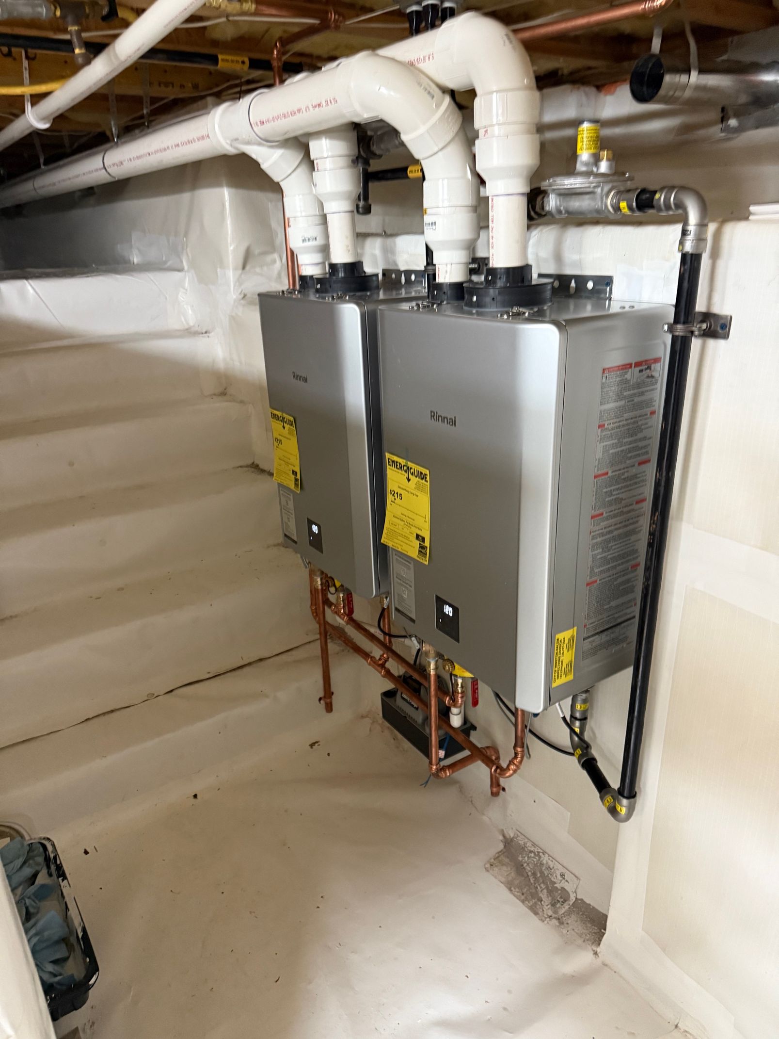 Two water heaters are sitting in a basement next to each other.