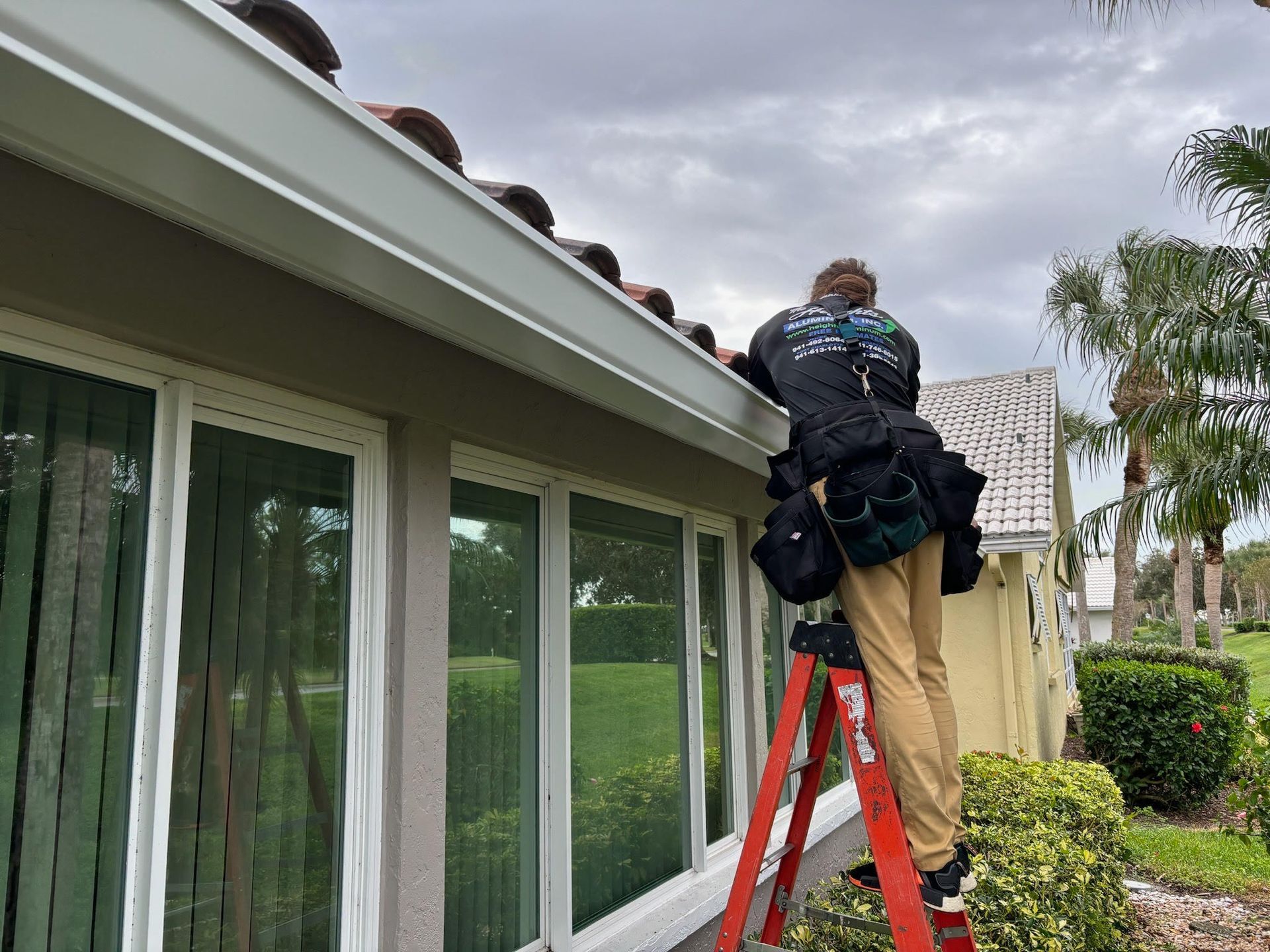 Person on ladder cleaning gutters on a house, overcast day.