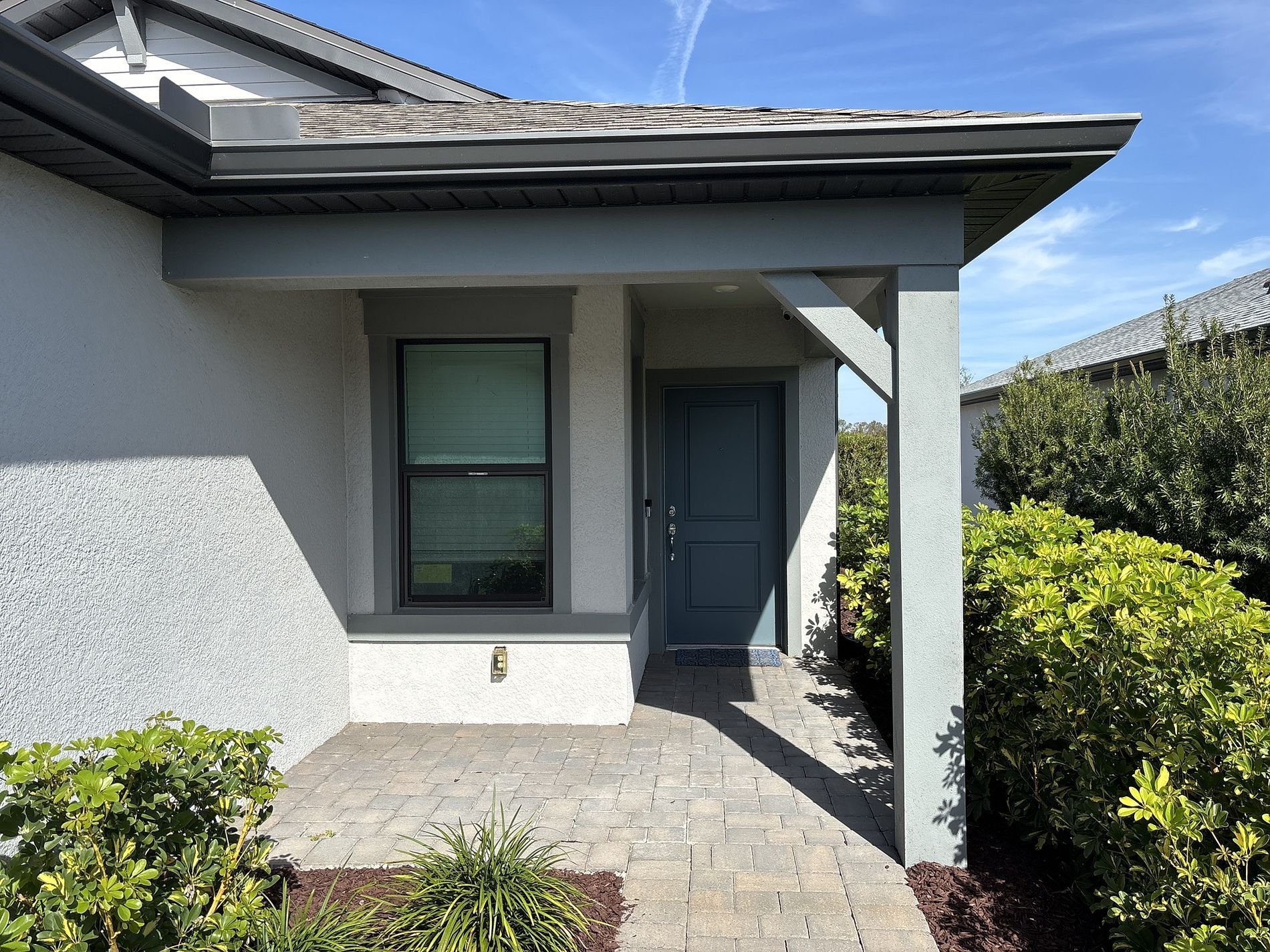 Entryway of a house with gray trim, a blue door, and a brick walkway.