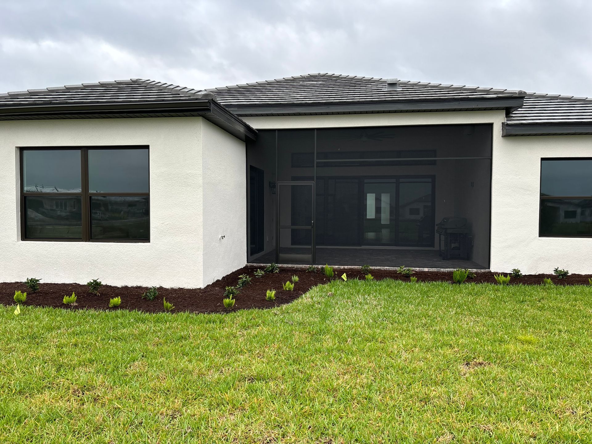 Exterior of a house with screened patio and manicured landscaping; overcast sky.