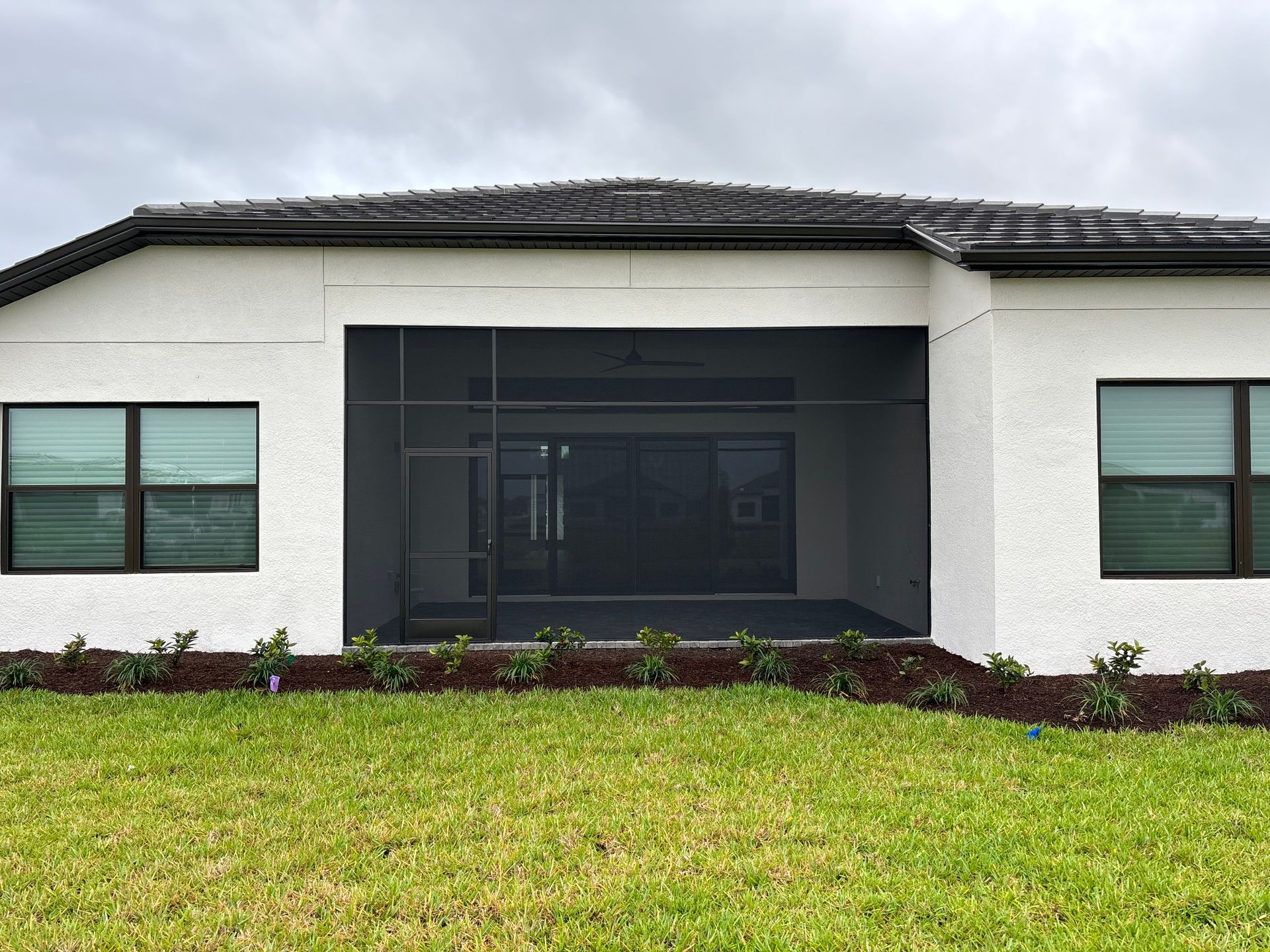 Backyard view of a house with a screened-in patio and green grass.