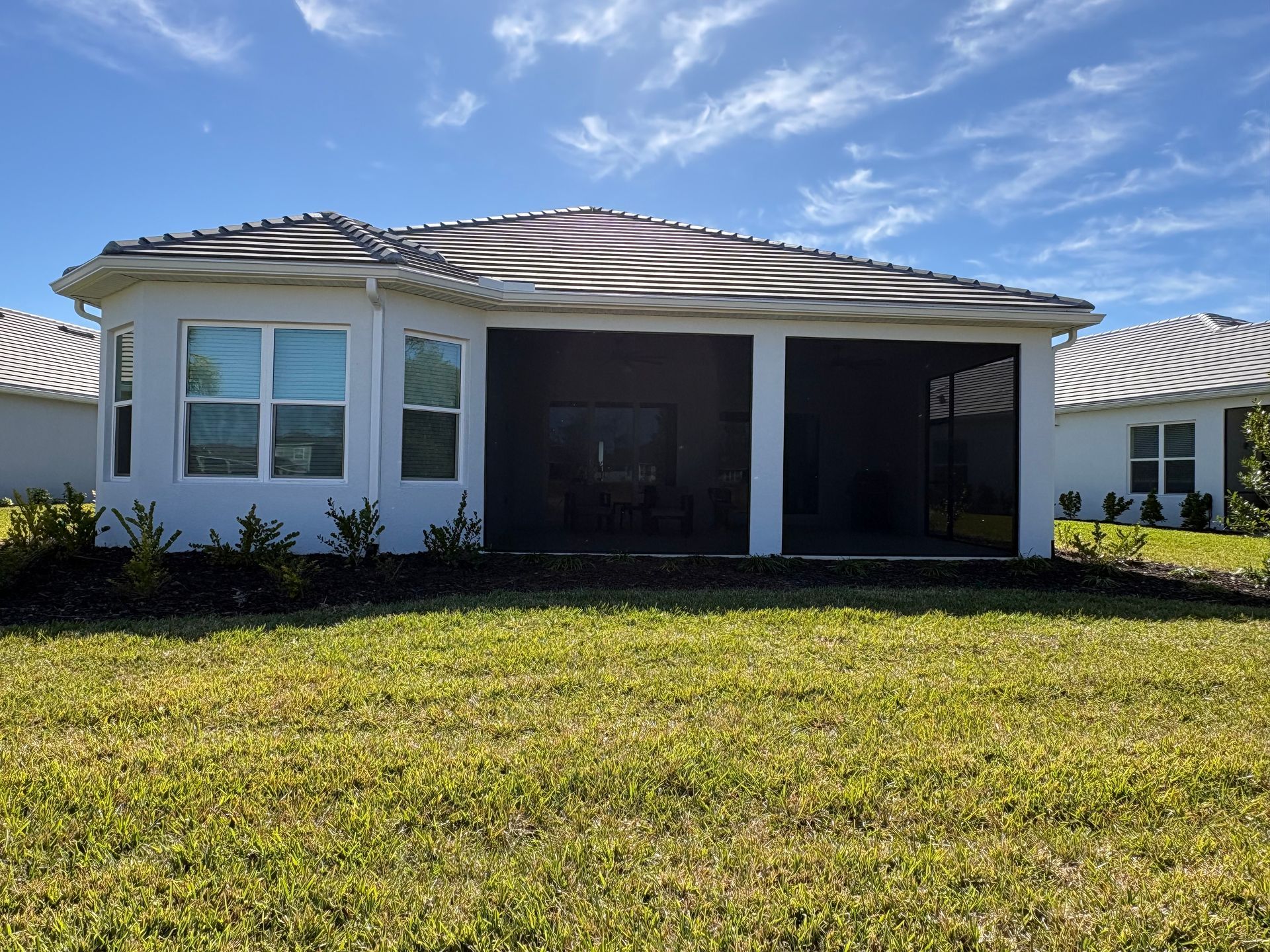 Back of a white house with screen-enclosed patio, surrounded by green grass and blue sky with clouds.