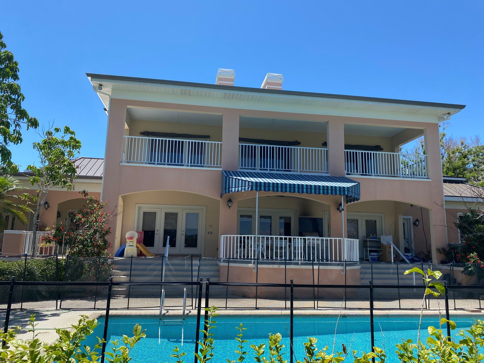 Two-story peach-colored house with balconies overlooking a swimming pool on a sunny day.