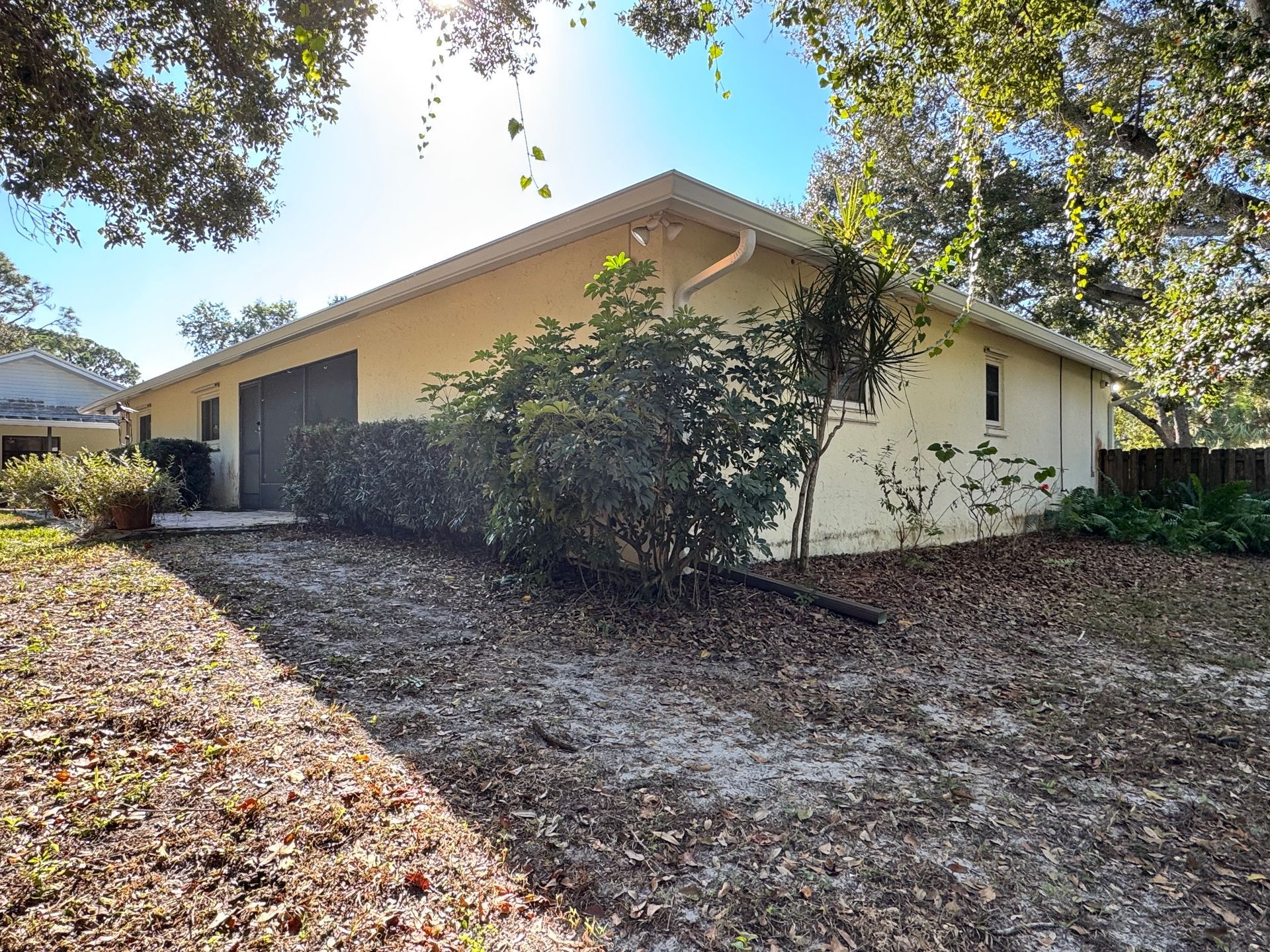 Beige house with a long, low roofline, surrounded by trees and dry vegetation.