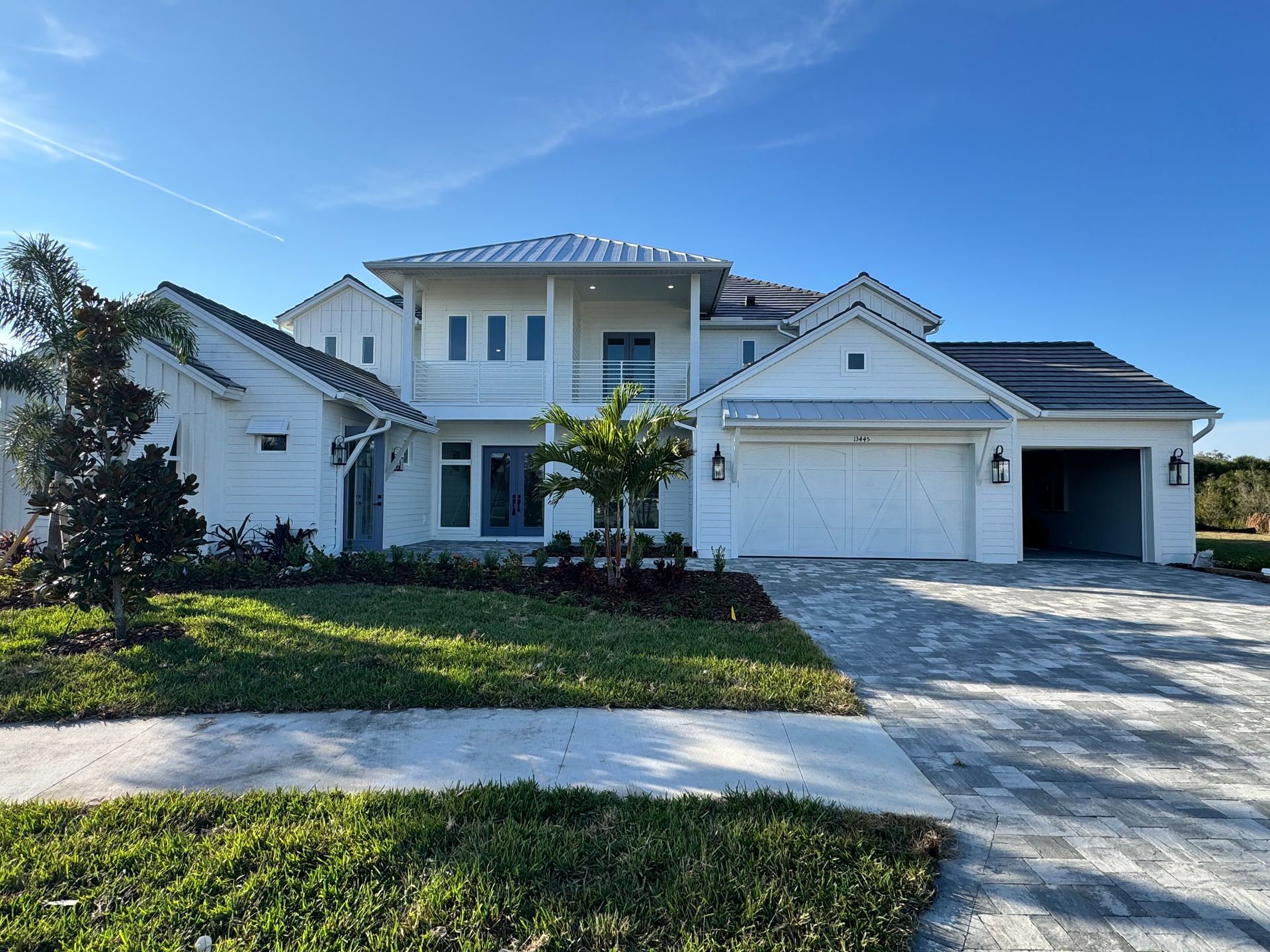 White two-story house with a blue sky, green lawn, and paver driveway.