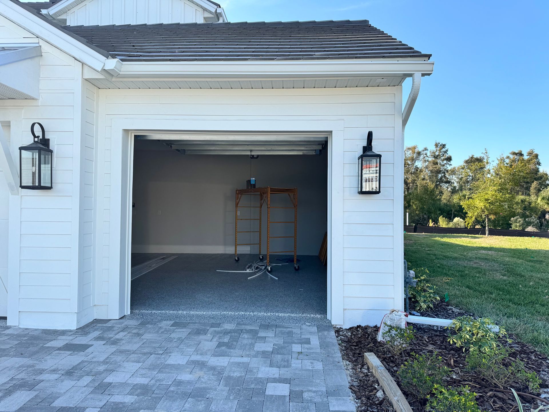White garage with open door, gray interior, black lanterns, paved driveway, blue sky.