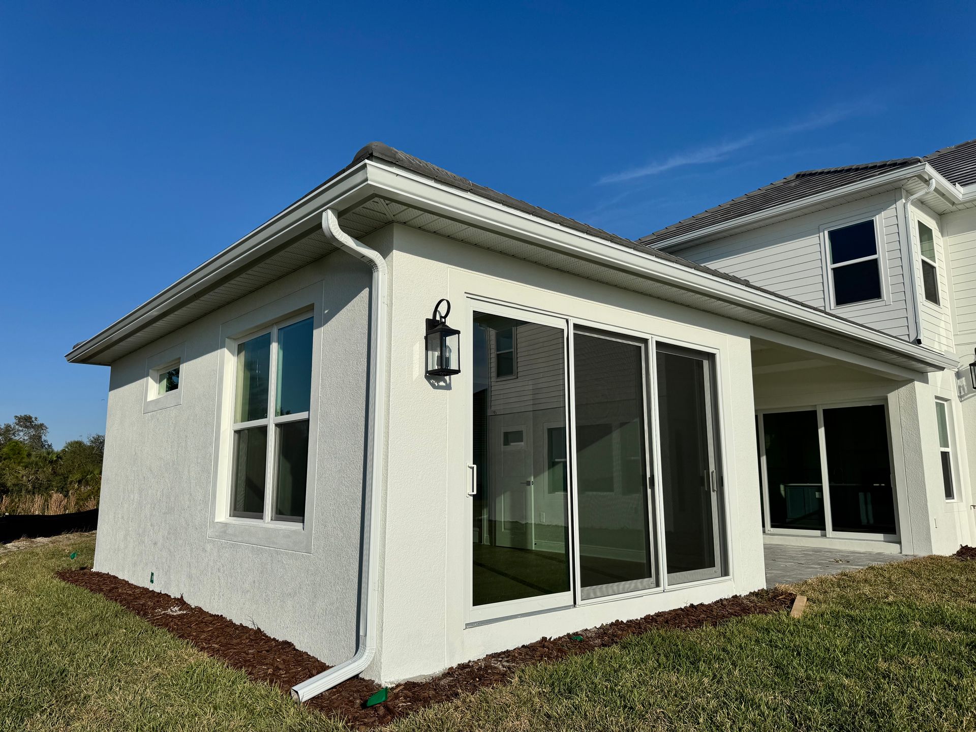 White stucco sunroom with sliding glass doors, connected to a two-story house, on a sunny day.