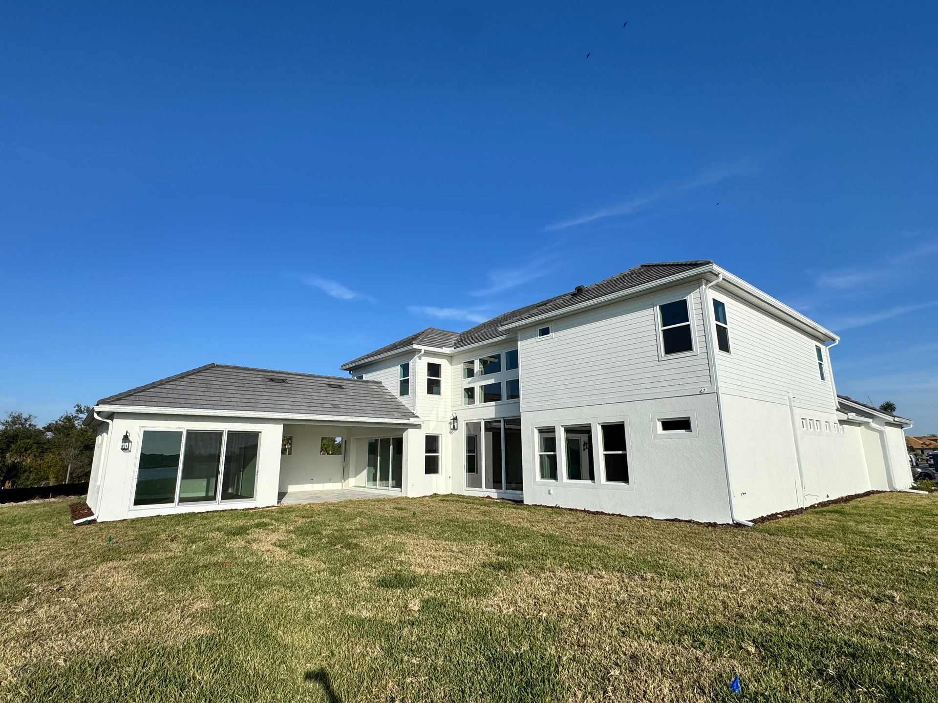 White two-story house with dark roof and windows, set against a blue sky, on a grassy lawn.