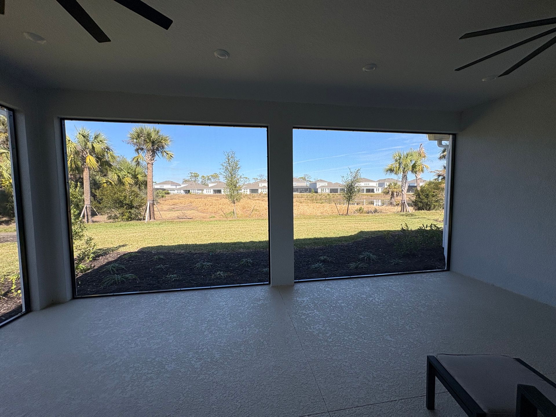 Interior view of a screened-in porch with a view of a grassy yard, trees, and blue sky.