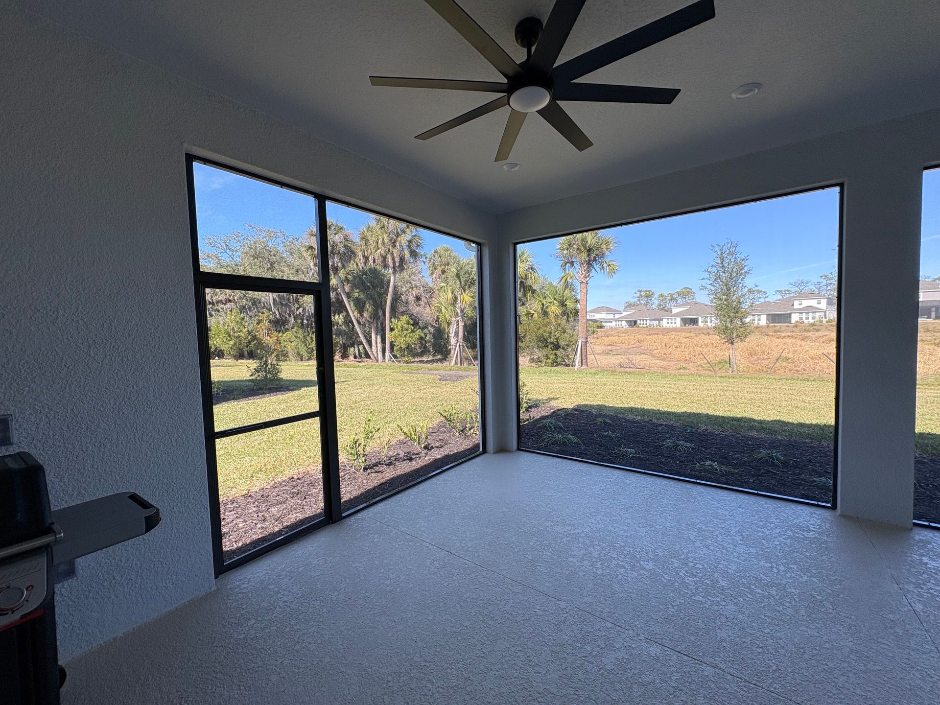 Sunroom with gray walls, black screened windows, and a view of a grassy yard under a blue sky.