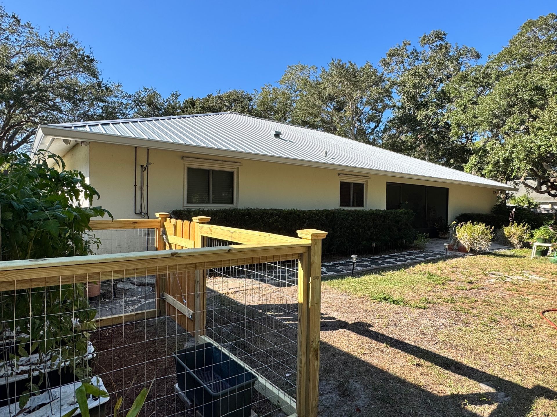 Beige house with a white roof, next to a wooden fence and garden.