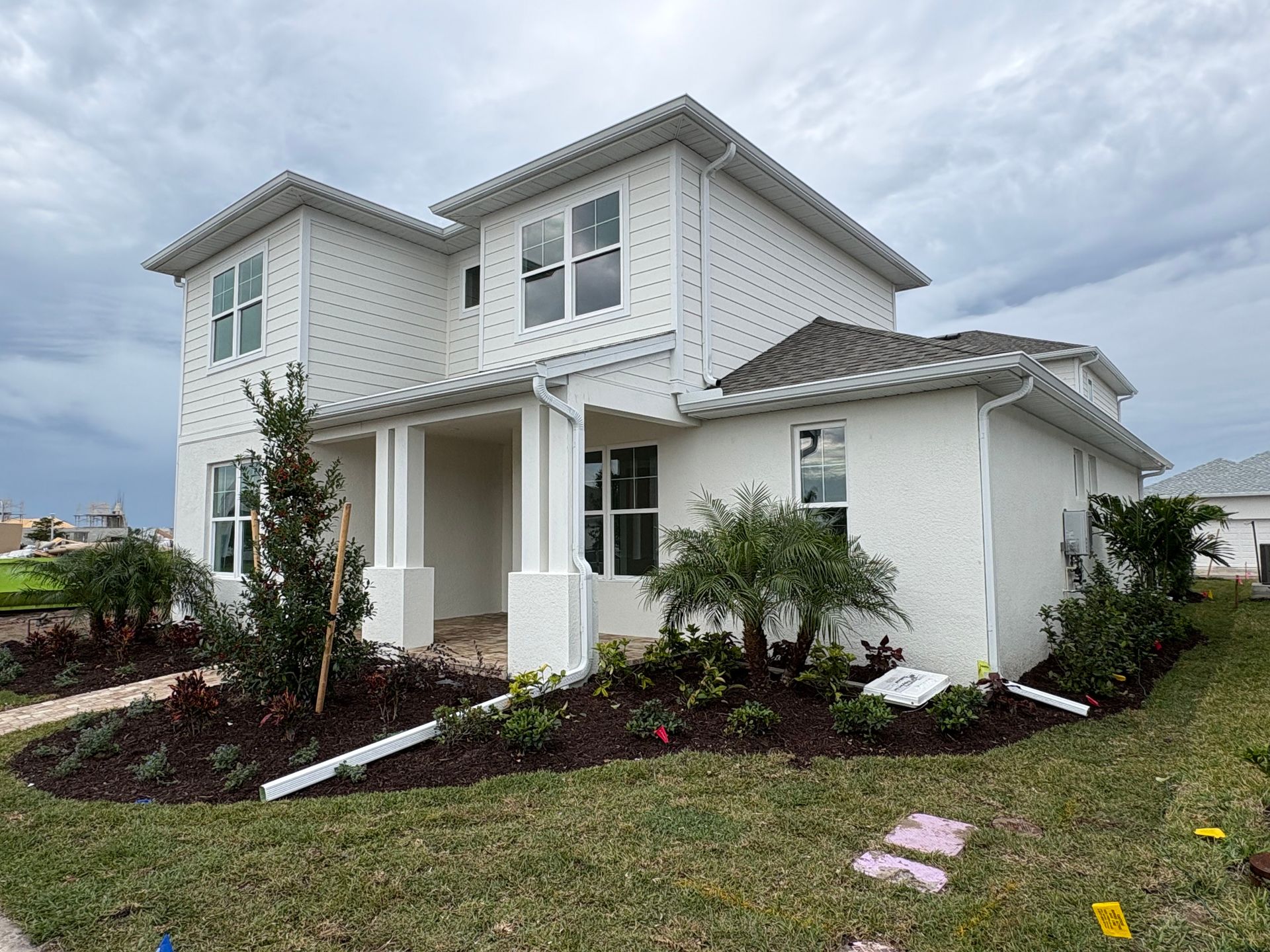 White two-story house with a porch and landscaping under a cloudy sky.