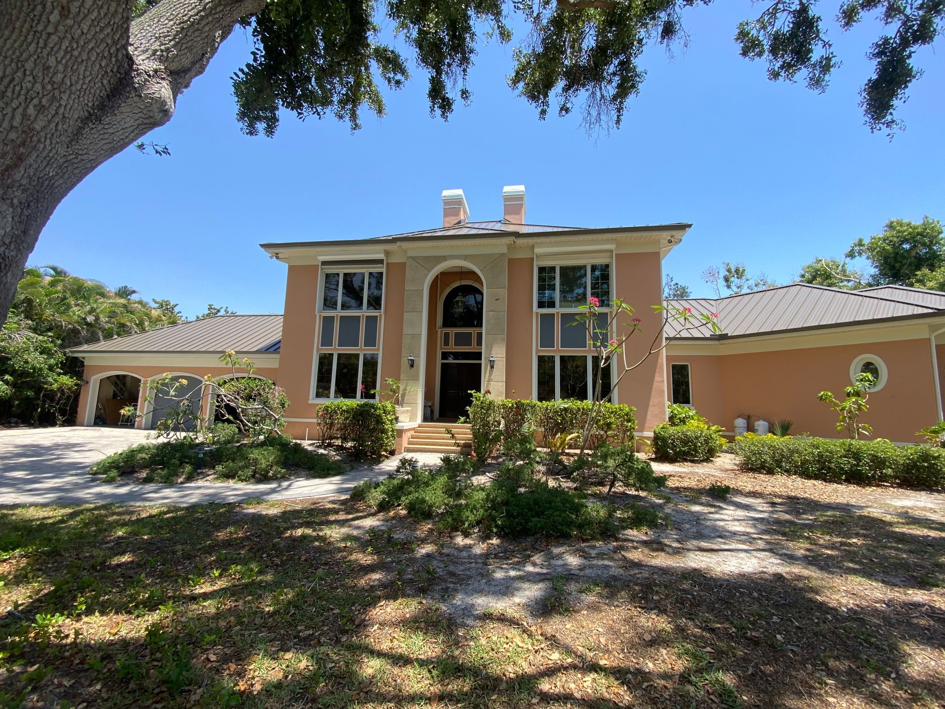 Tan stucco house with large windows, arched entryway, and two chimneys under a blue sky.