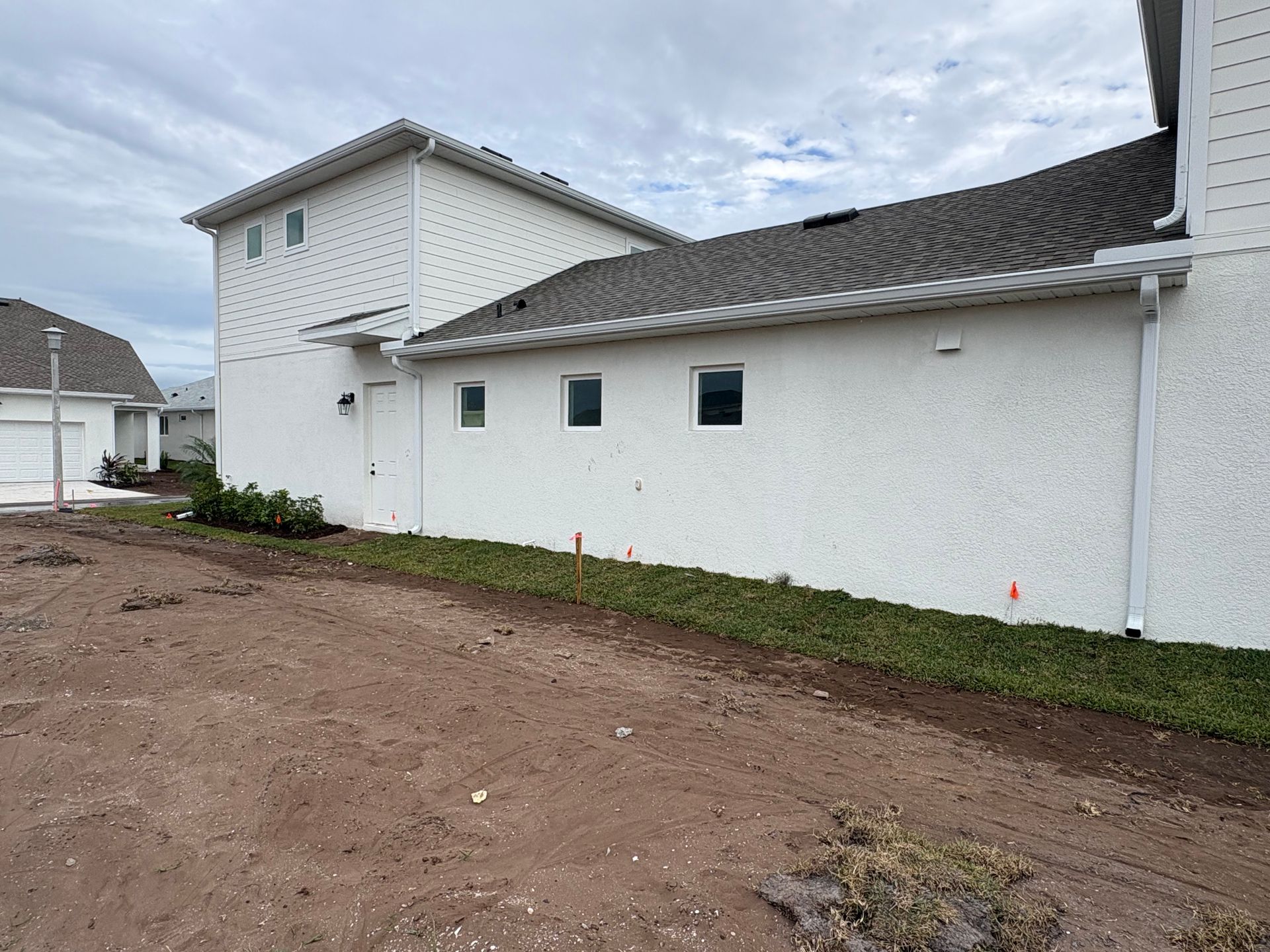 Side view of a two-story white house under construction with a cloudy sky.
