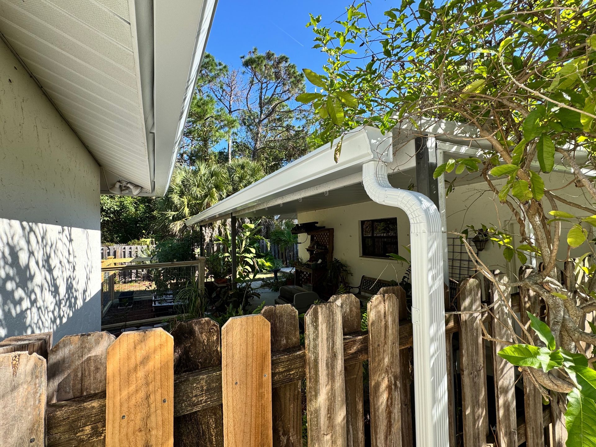 White gutter on a house with a weathered wooden fence in the foreground.