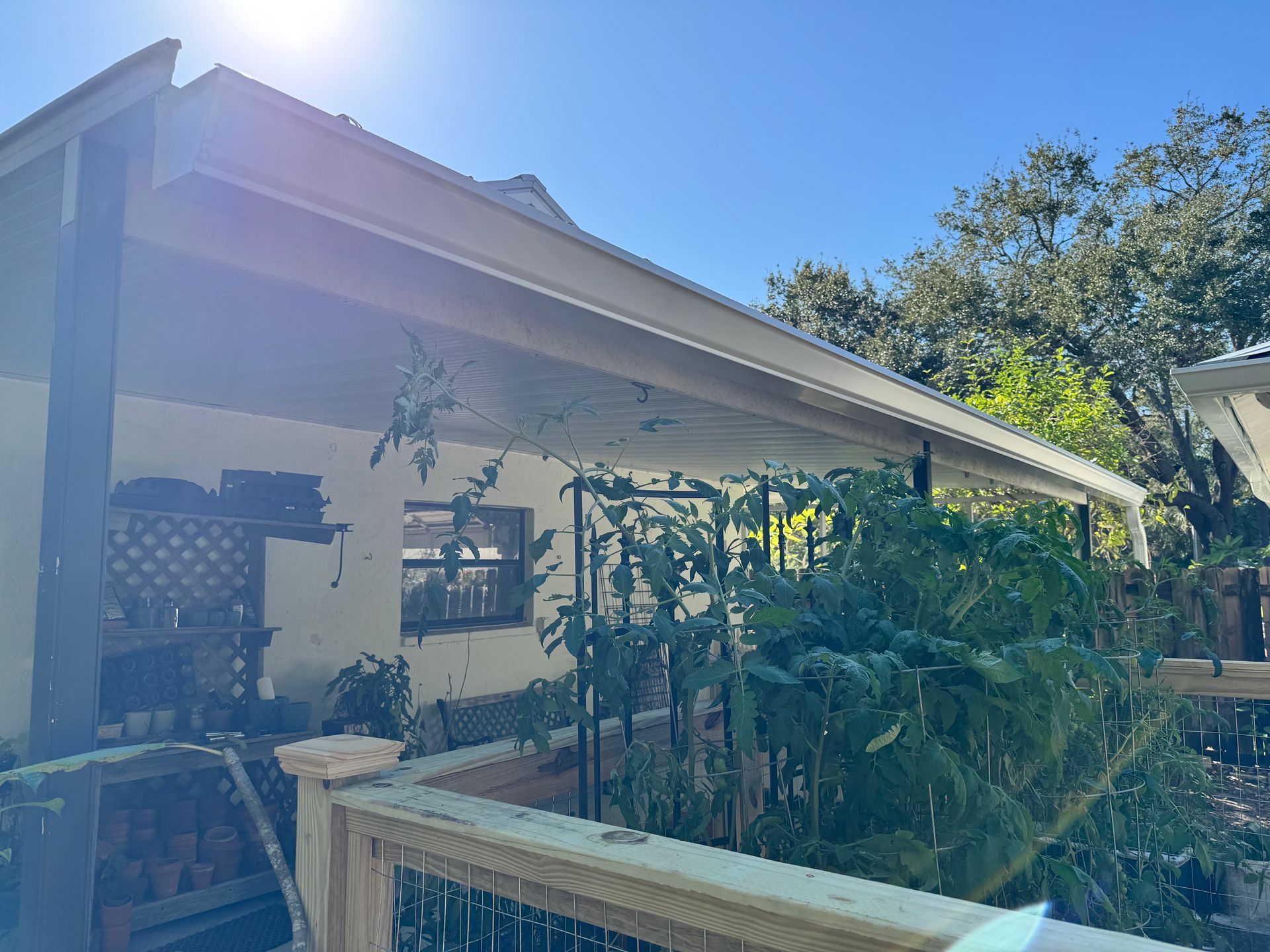 Covered porch of a house with a wooden railing and a garden of plants. Sunlight.