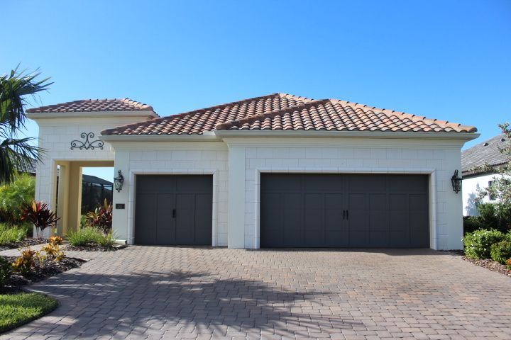 Two-car garage with gray doors, tan stucco, and red tile roof; brick driveway and blue sky.