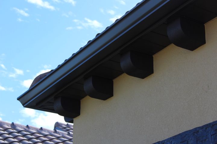 Dark brown eaves and guttering on a tan stucco building with dark blue sky.