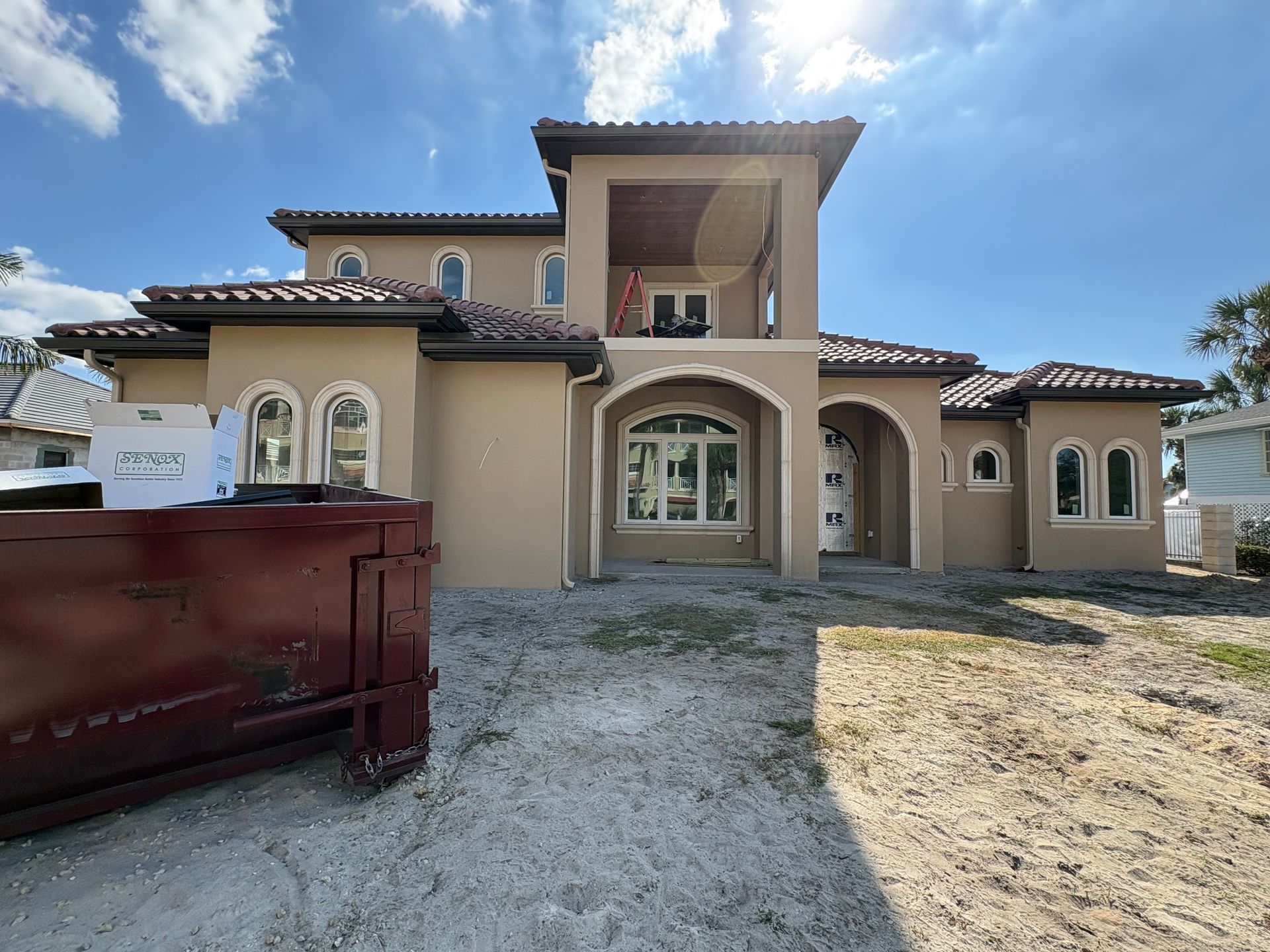 Beige stucco house with arched windows and a red tile roof; construction debris in front.