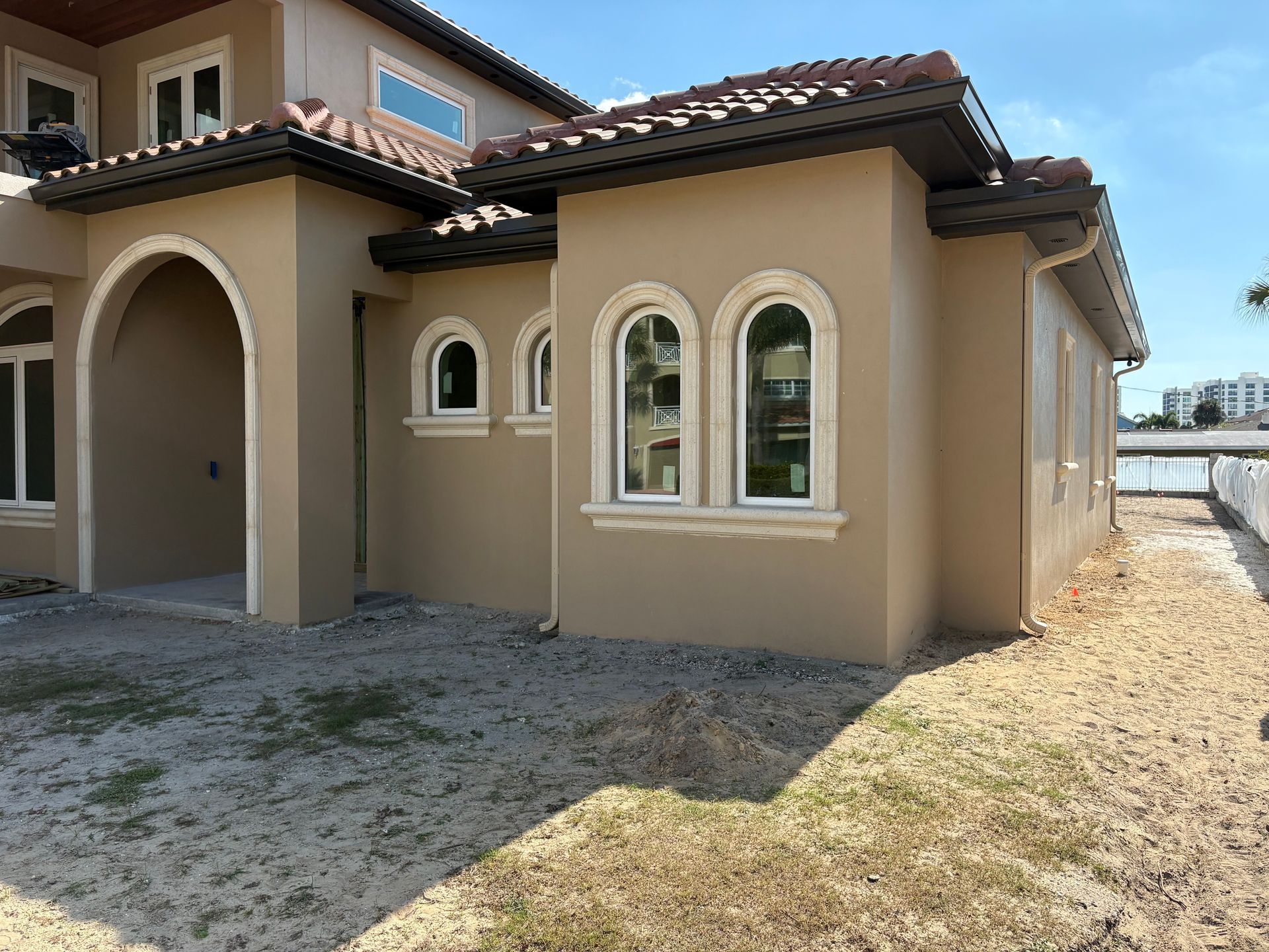 Beige stucco home with terracotta roof tiles and arched windows on a sunny day.