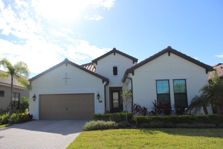 White stucco house with brown roof and garage door, blue windows, and green grass.