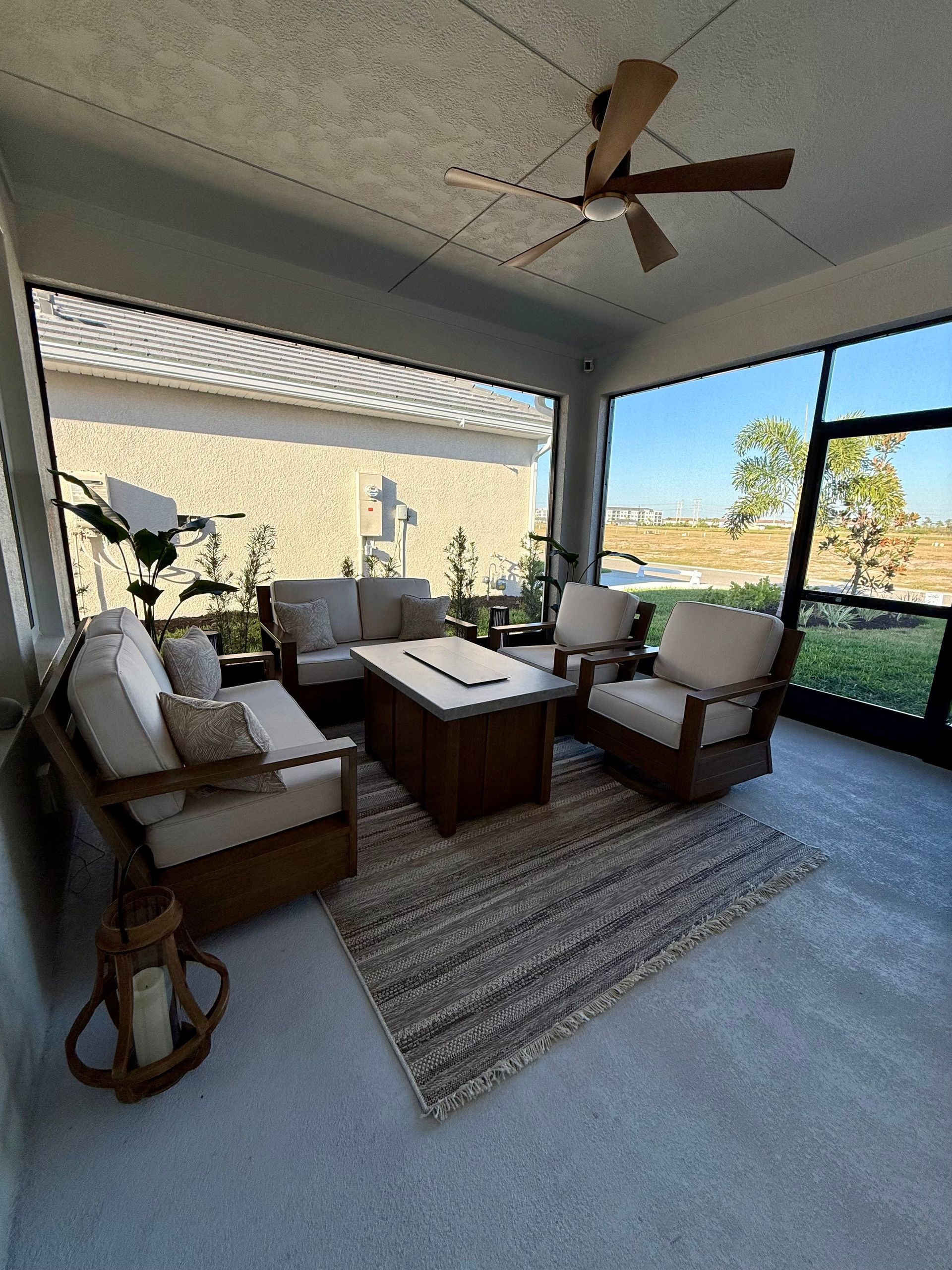 Screened-in patio with light-colored wood furniture, neutral rug, and ceiling fan, overlooking a yard on a sunny day.