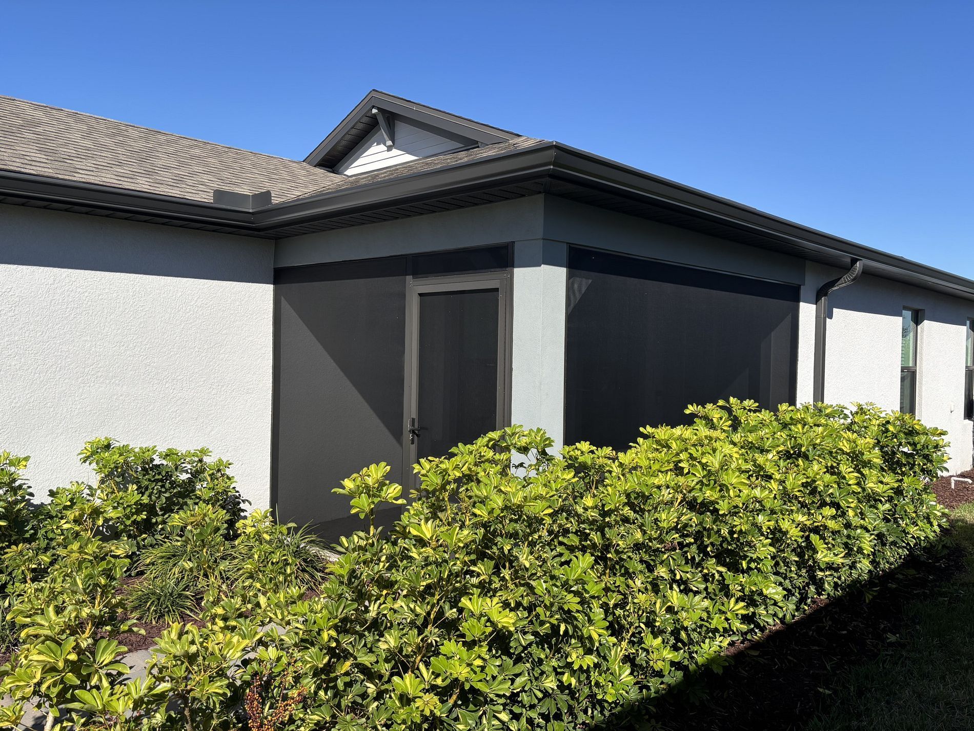 Exterior view of a home with grey siding, dark shutters and landscaping. Clear blue sky.